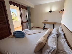 A bedroom with a bed, pillows, a bedside table with a globe, a window with blinds, and a view of greenery outside. - Authentic apartment, 2 lovely private balconies (Albufeira)