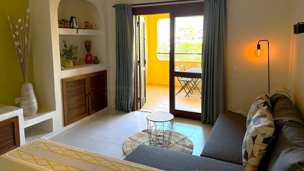 Un salon comprenant un canapé, une petite table ronde, un balcon avec une table et des chaises, et une lampe fixée au mur.