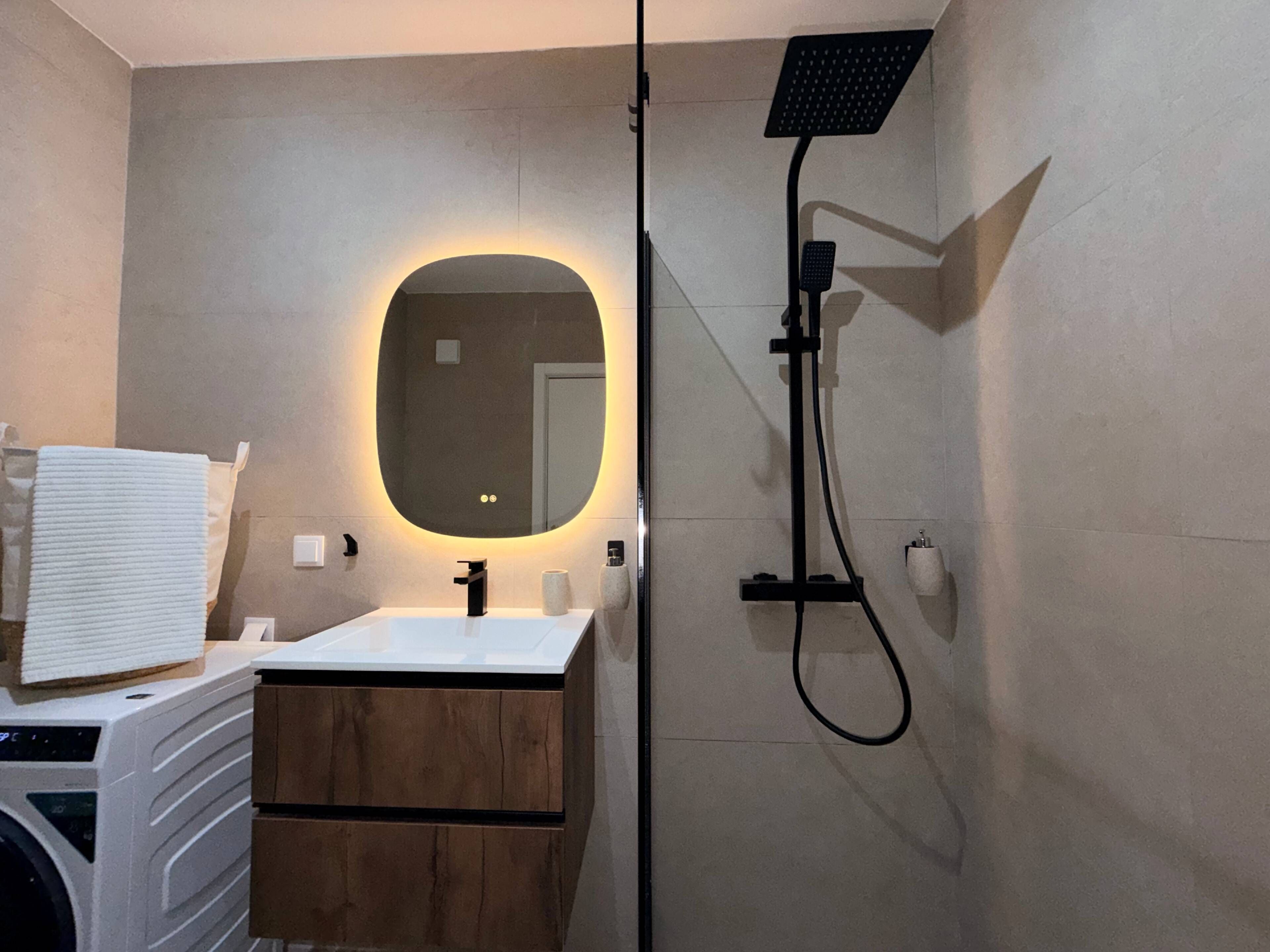 Een moderne badkamer met een ronde spiegel, een handdouche en een witte wastafel.
