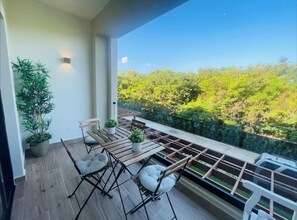 Ein Balkon mit Holztisch und Stühlen, Blumentöpfen und Blick auf Gr ünflächen.