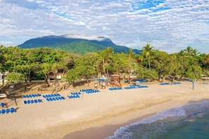 Ein Strand mit Reihen blauer Liegestühle, Palmen und einem Berg im Hintergrund.