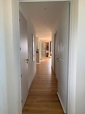 A hallway with wooden flooring and white doors, leading to a room with a bookshelf and a window. - Family apartment with sea view 500m from the sea (Albitreccia)