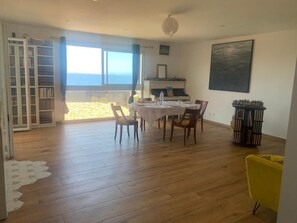A dining area with a table set for four, a bookshelf, a piano, and a view of the sea. - Family apartment with sea view 500m from the sea (Albitreccia)