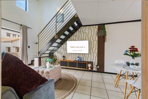 Ein modernes Wohnzimmer mit Treppe, einer Couch, einem Couchtisch und einem Essbereich mit Stühlen und Tisch.