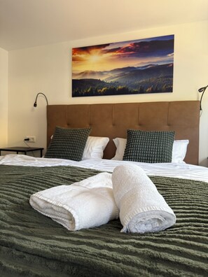 Une chambre d’hôtel avec un lit, une tête de lit, une table de chevet, une lampe et un tableau représentant un coucher de soleil.
