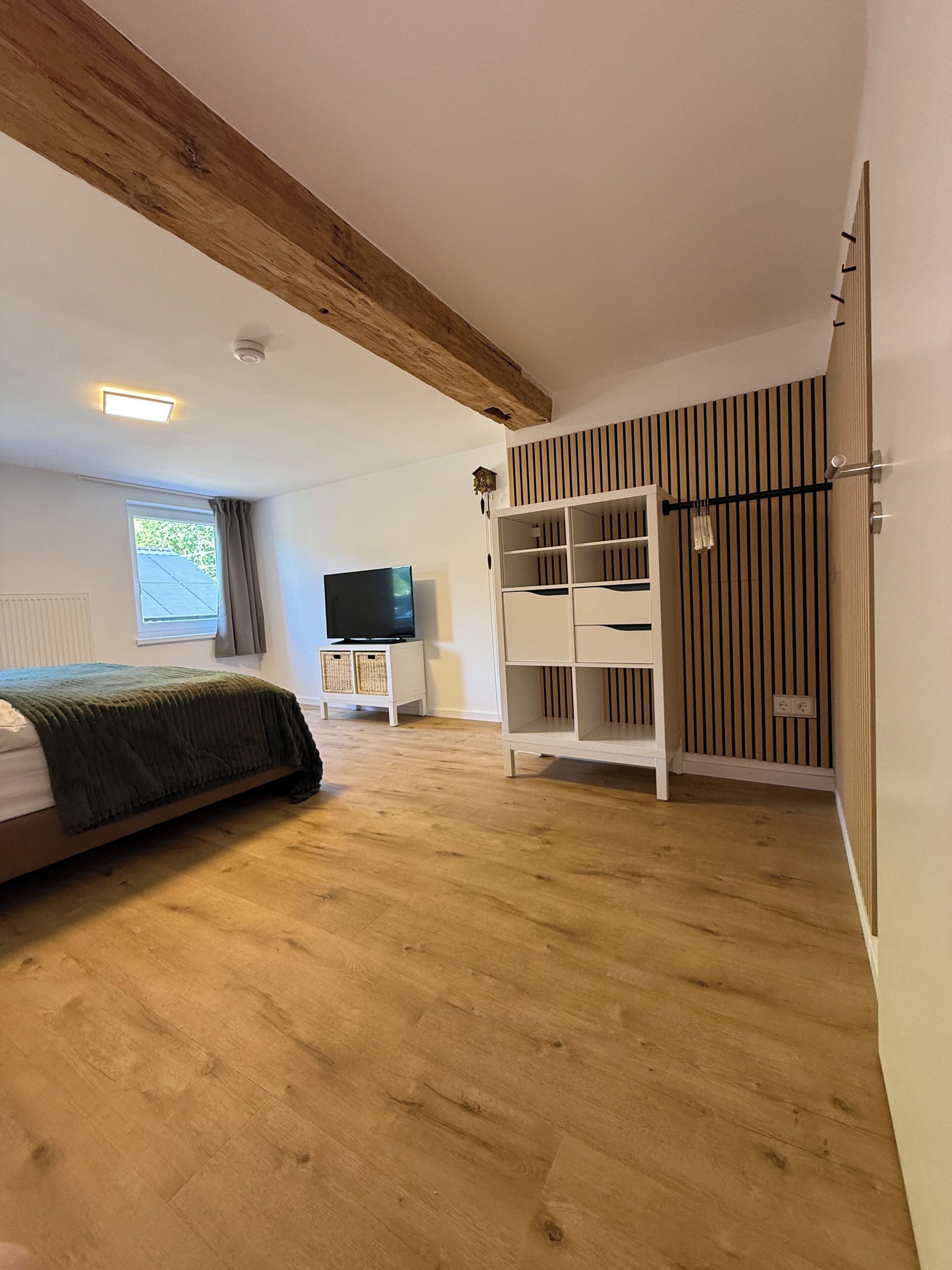 Ein Schlafzimmer mit Bett, Fernseher, Kleiderschrank und einem Fenster mit Vorhängen.