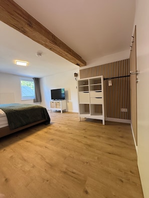 Ein Schlafzimmer mit Bett, Fernseher, Kleiderschrank und einem Fenster mit Vorhängen.