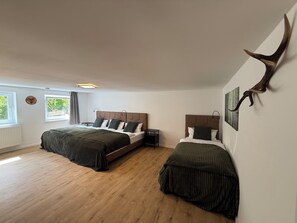 Ein Schlafzimmer mit zwei Betten, Holzboden, einem Fenster und einem an der Wand befestigten Hirschkopf.