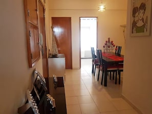 A dining area with a table set for four, a refrigerator, and a door leading to another room. - Delgado Airport Suite (Lisbon)