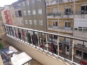 A multi-story residential building with balconies, a tiled floor, and a small table with a chair. - Delgado Airport Suite (Lisbon)