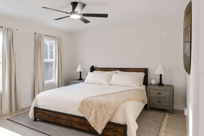 Ein Schlafzimmer mit Bett, Nachttischen, Deckenventilator und einem Fenster mit Vorhängen.