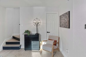 Eine Treppe führt zu einer Empore, dort befindet sich ein schwarzer Schrank mit einer Pflanze, ein Sessel und ein an der Wand hängendes abstraktes Gemälde.