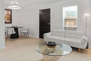Ein modernes Wohnzimmer mit einem Glastisch, einem weißen Sofa, einem Esstisch mit Stühlen und einer Tür.