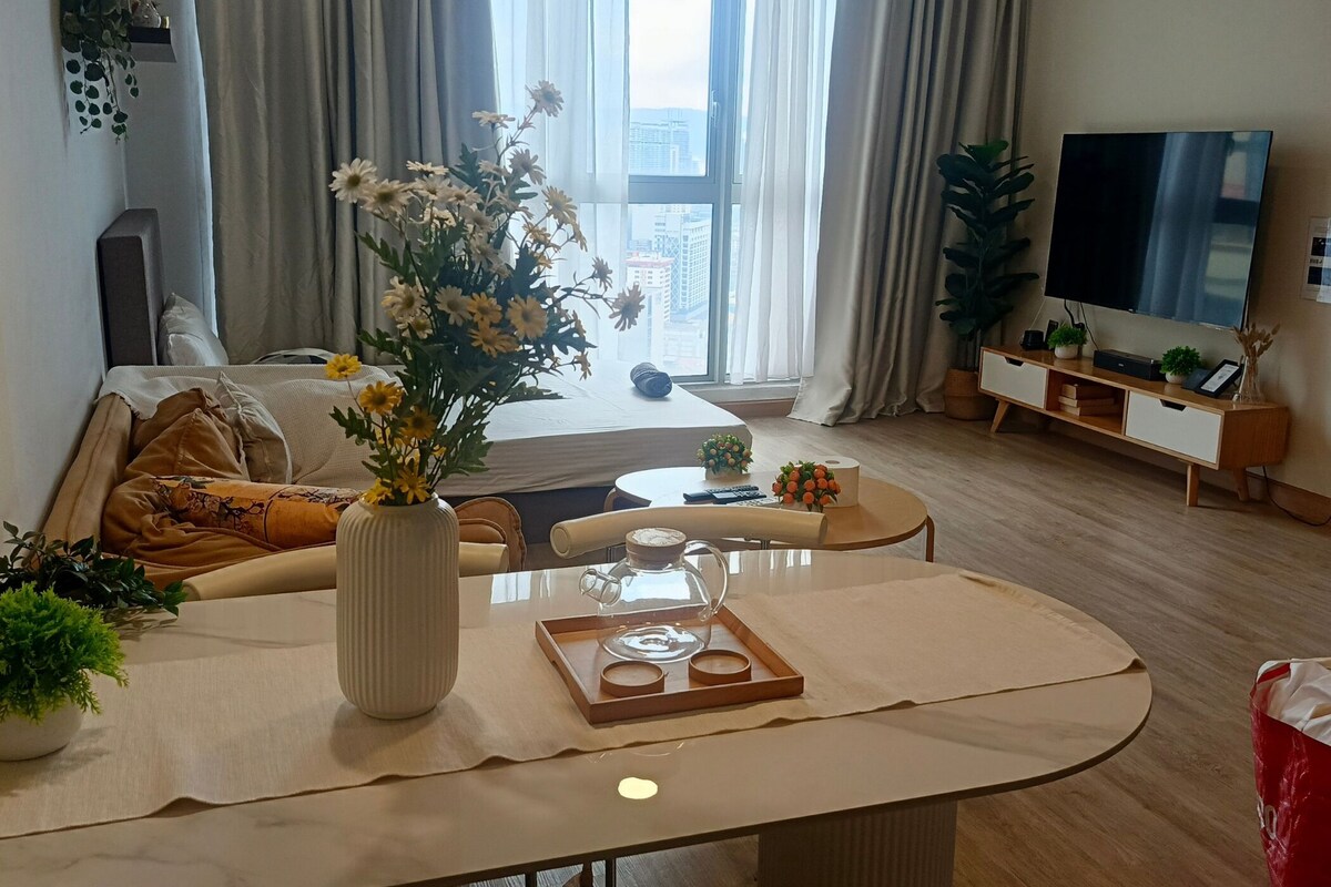 Uma sala de estar moderna com um sofá, uma mesa de centro, uma TV e uma janela grande com cortinas.