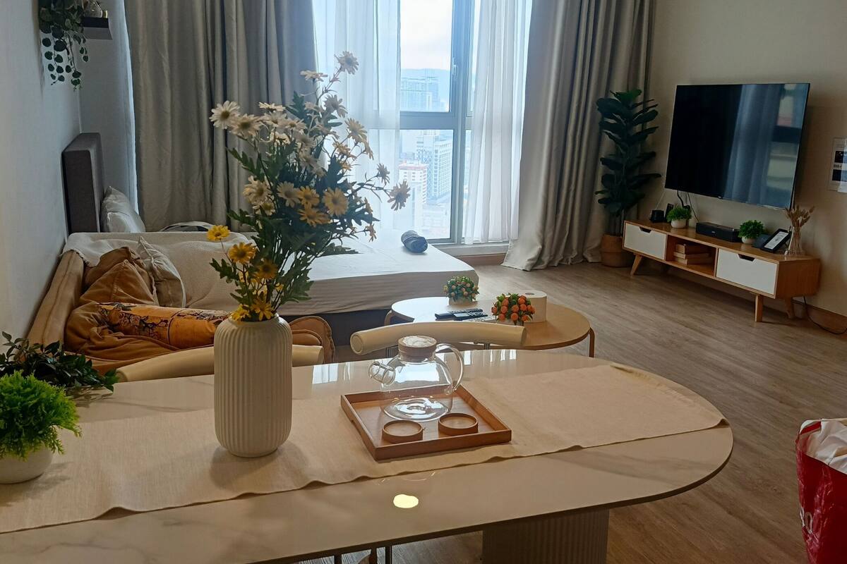 Un salon moderne avec un canapé, une table basse, un téléviseur et une grande fenêtre avec des rideaux.