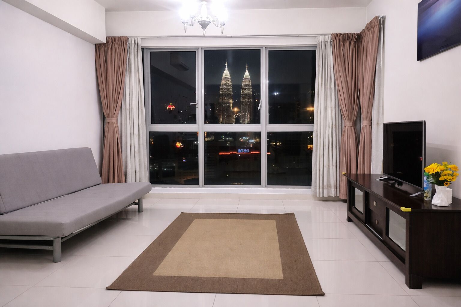 A living room with a sofa, a TV, a rug, and a window with a cityscape view.