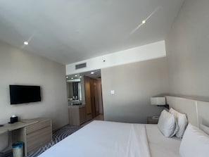 Ein Hotelzimmer mit Bett, Schreibtisch, Fernseher, Spiegel und einer Tür zu einem Badezimmer.
