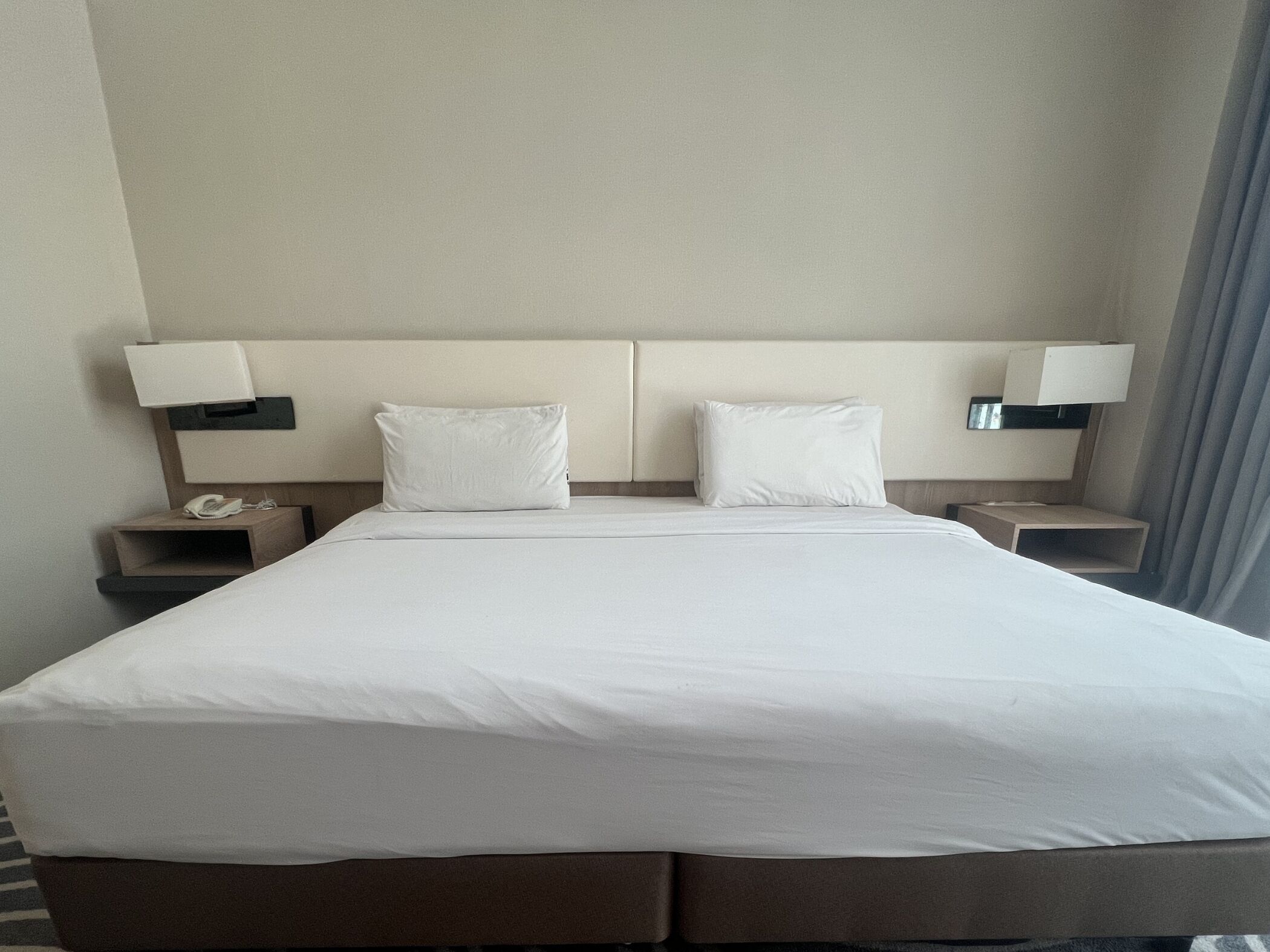 A hotel room with a large bed, two bedside tables, a lamp on each table, and a phone on one of the tables.