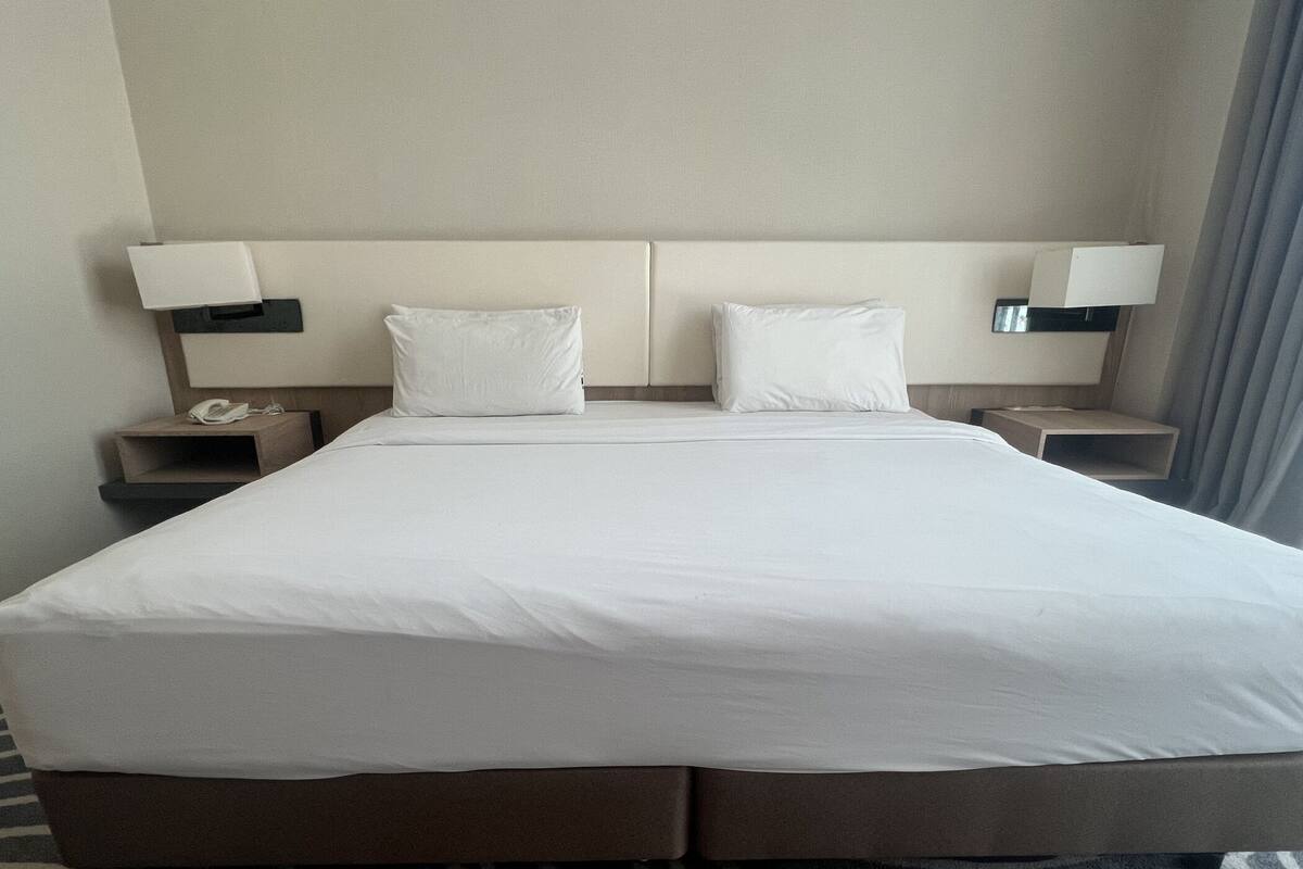 Une chambre d’hôtel avec un grand lit, deux tables de chevet, une lampe sur chaque table et un téléphone sur l’une des tables.