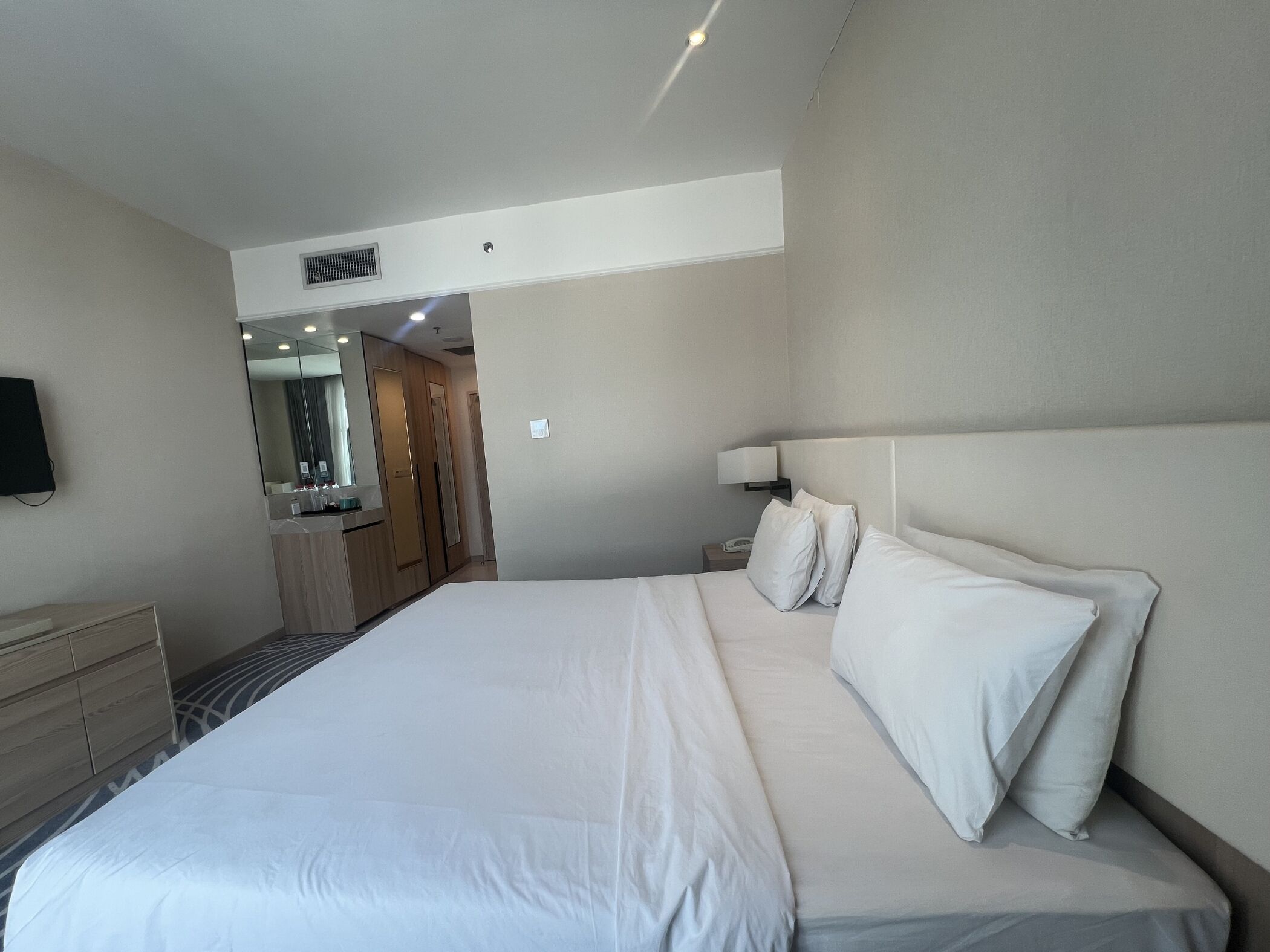 A hotel room with a large bed, a bedside table, a lamp, a mirror, and a wardrobe.