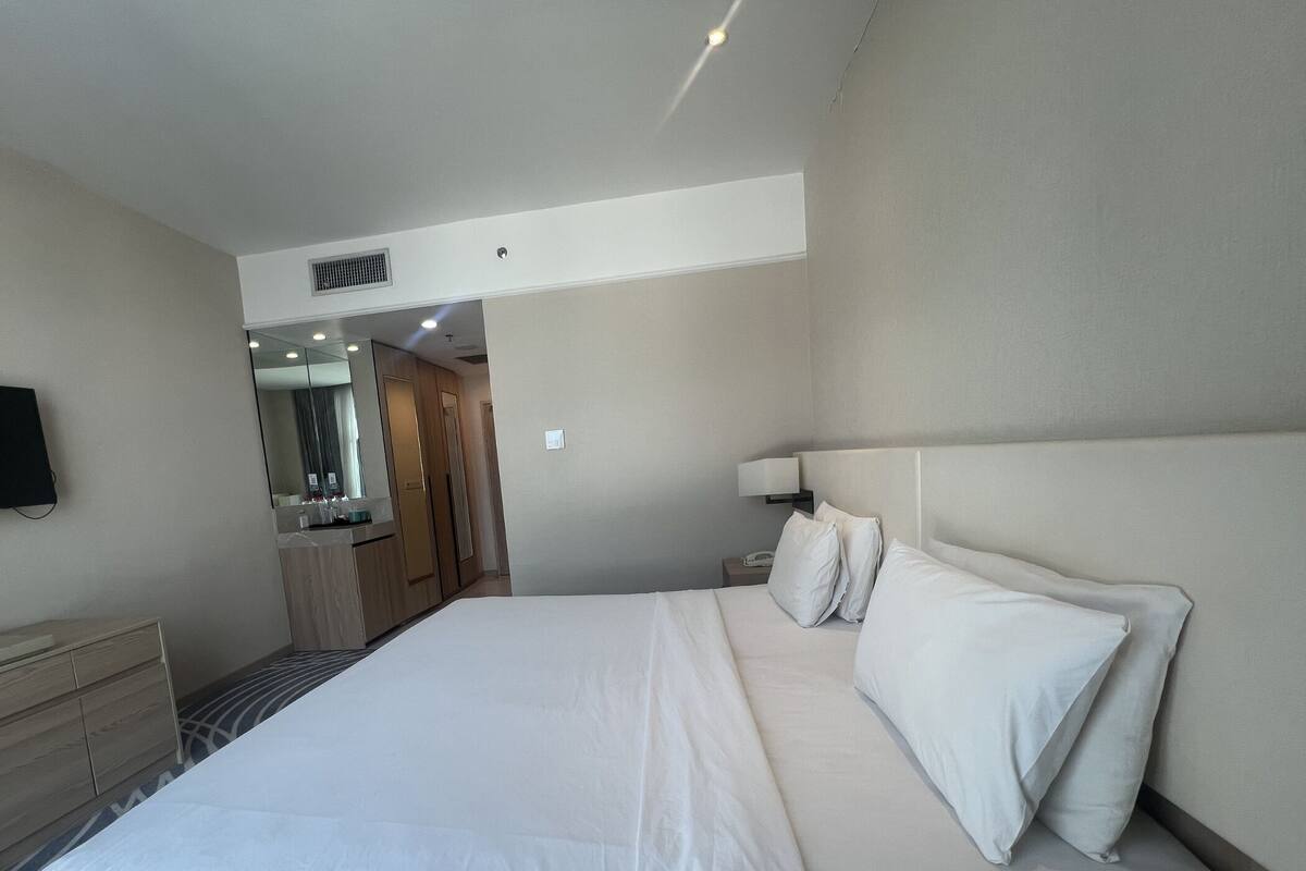 Une chambre d’hôtel avec un grand lit, une table de chevet, une lampe, un miroir et une armoire.