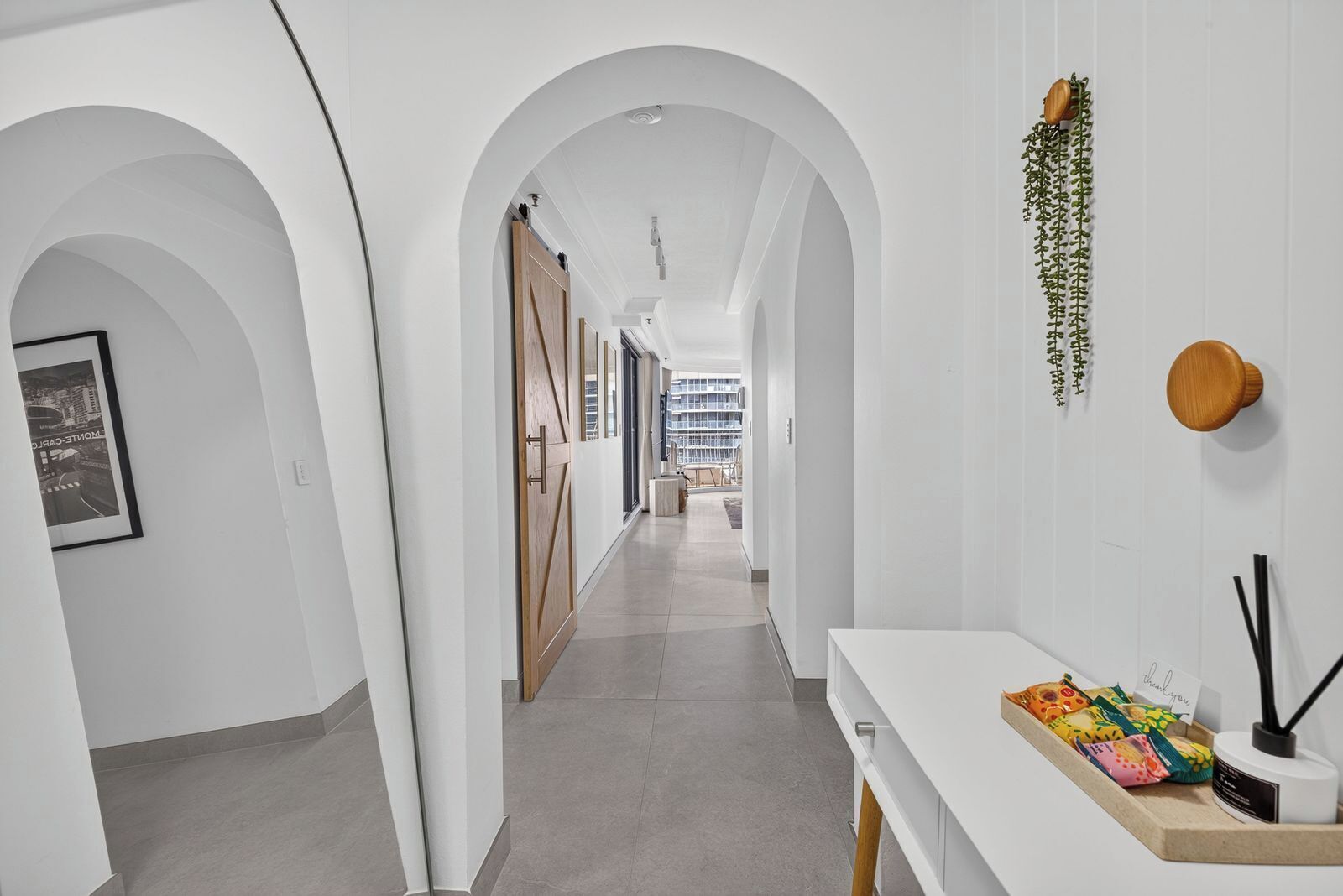 A hallway with white walls, arched doorways, and a white reception desk with a plant and a card holder.