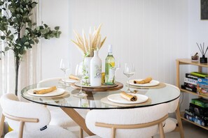 A round glass table with white chairs, a white vase with dried plants, a bottle of gin, and a glass of wine. - Ocean-View 2BR Walk to Beach, Dining & Rail (Surfers Paradise)
