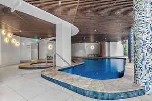 An indoor swimming pool with a tiled edge, a wooden ceiling, and a tiled wall on one side. - Ocean-View 2BR Walk to Beach, Dining & Rail (Surfers Paradise)