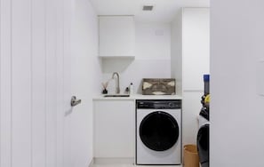 A compact laundry room with a washing machine, a sink, and a cabinet. - Ocean-View 2BR Walk to Beach, Dining & Rail (Surfers Paradise)