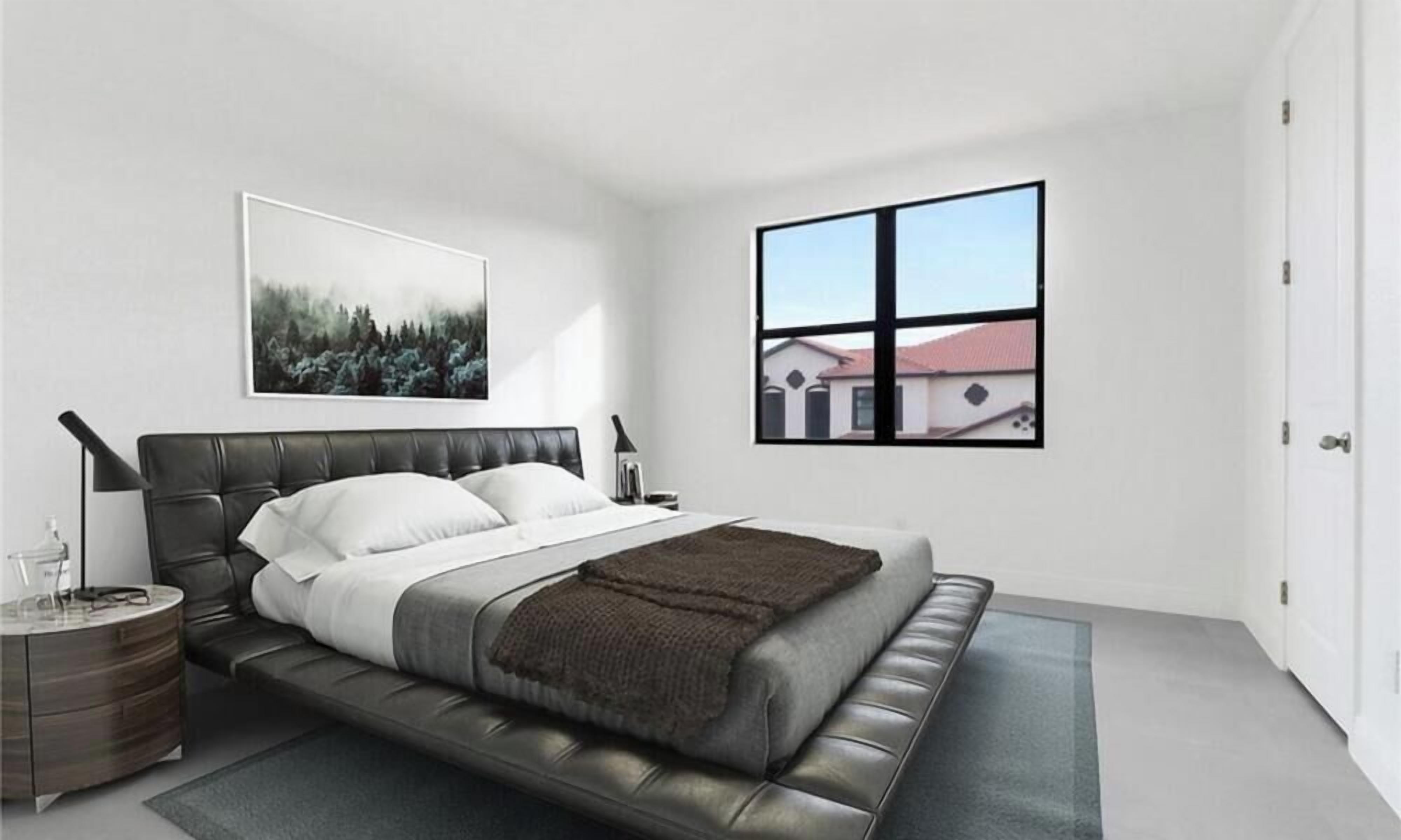 A modern bedroom with a large bed, a bedside table, a nightstand, a window with a view, and a framed picture on the wall.