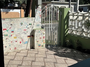 A gate with a wall covered in various writings and flags, leading to a building with a green facade.
