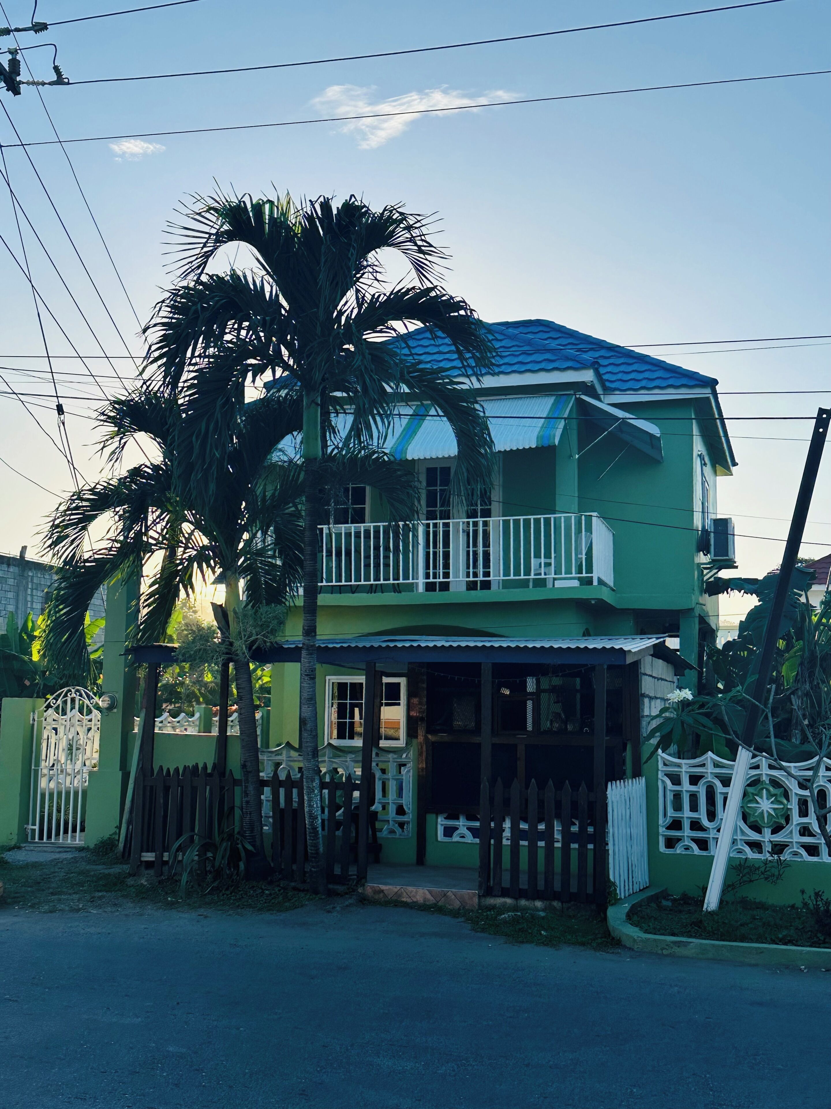 A two-story house with a balcony, a gated entrance, and a palm tree.. Cozy studio in tranquil Ocho Rios with refreshing A/C with a wonderful loft bed!