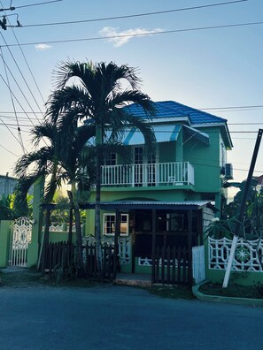 Une maison à deux étages avec un balcon, une entrée fermée par un portail et un palmier.