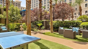 A courtyard with a ping pong table, outdoor seating, and palm trees.