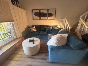 Una sala de estar con un sofá modular, un otoman redondo y un ventanal con vistas.