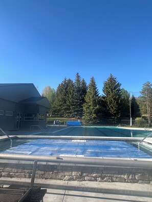 Una piscina con pared de piedra y barandillas de metal, rodeada de árboles y un edificio.
