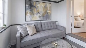 A modern living room with a grey sofa, a glass coffee table, and a large abstract painting on the wall. - Cozy 2BR Apartment  Parking Included (London)