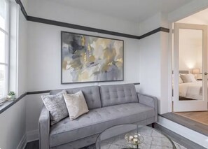 Ein modernes Wohnzimmer mit einem grauen Sofa, einem Glastisch und einem großen abstrakten Gemälde an der Wand.