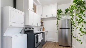 A kitchen with white cabinets, a stainless steel refrigerator, a washing machine, and a wooden floor. - Cozy 2BR Apartment  Parking Included (London)