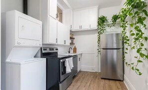 Eine Küche mit weißen Schränken, einem Edelstahl-Kühlschrank, einer Waschmaschine und Holzboden.