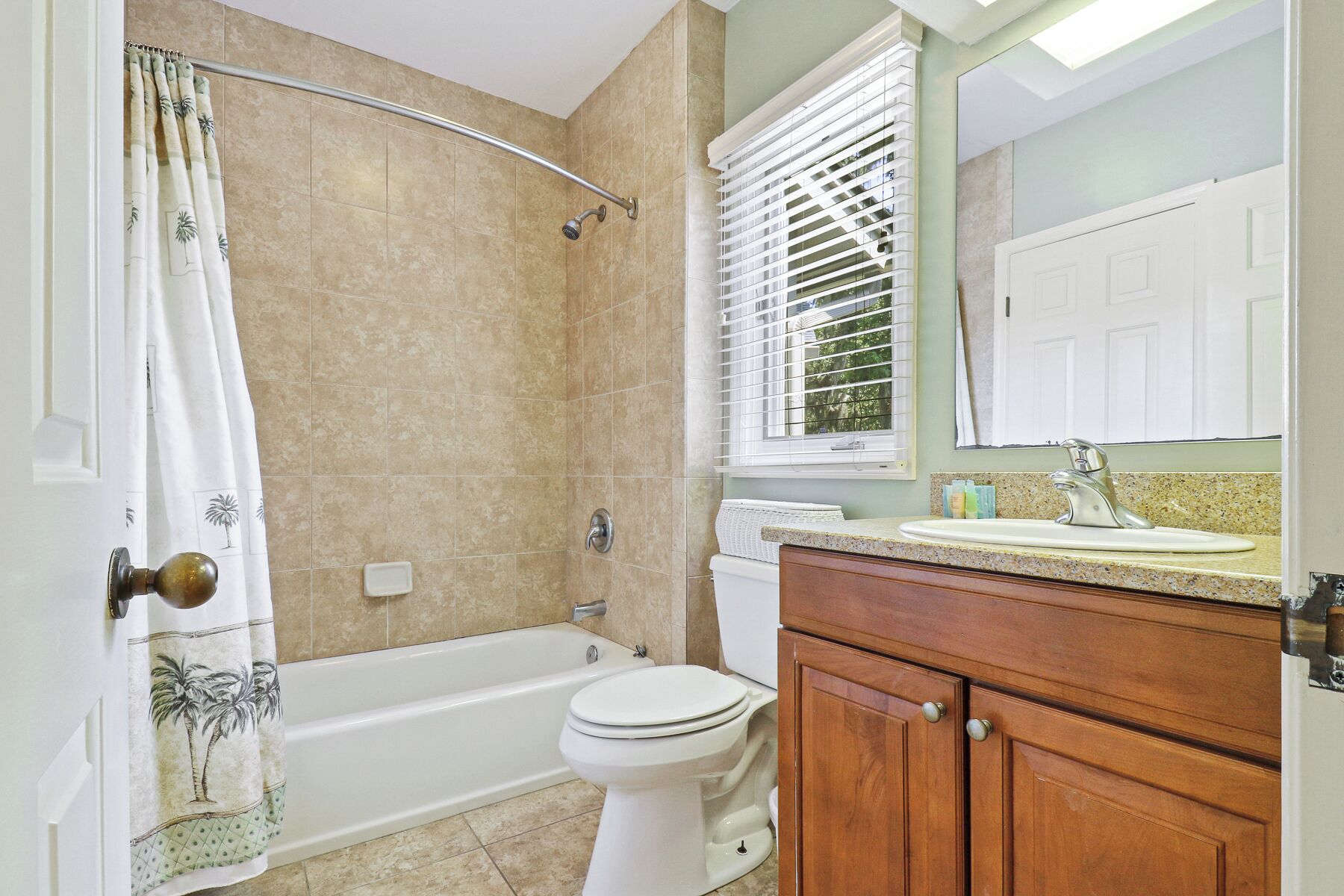 A bathroom with a bathtub, toilet, vanity, and a window with blinds.
