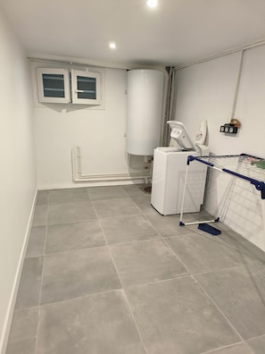 Une buanderie Ă©quipĂ©e dâun lave-linge, dâun sĂšche-linge et dâune planche Ă repasser.