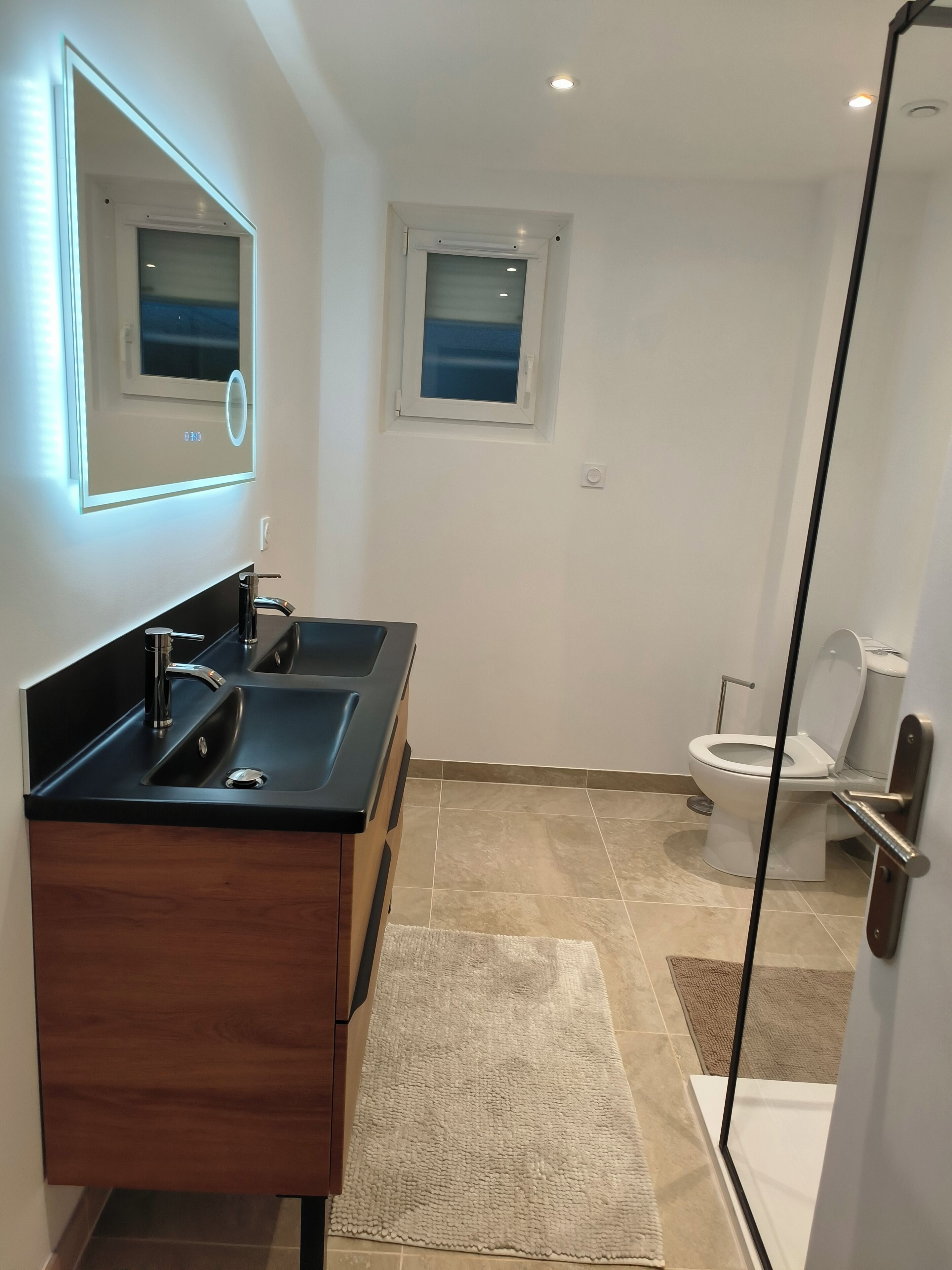 Un baño moderno con lavamanos de superficie negra, espejo, inodoro y zona de ducha.