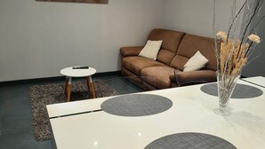 Una sala de estar moderna con un sofá marrón, una mesa de centro blanca y una mesa de comedor con manteles individuales grises.