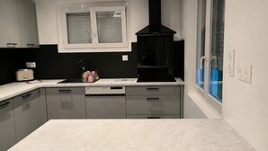 Una cocina moderna con una isla grande, dos taburetes de bar, una campana extractora negra y una ventana con persianas.