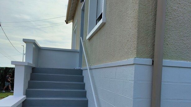 Un conjunto de escaleras exteriores que conducen a un edificio con fachada texturizada y una ventana con persianas cerradas.