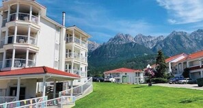 A multi-story building with balconies, a red-tiled roof, and a view of mountains.