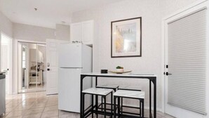A kitchen with a white refrigerator, a small table with two chairs, a framed picture on the wall, and a closed door. - SUNCHASER VACATION VILLAS / RIVERSIDE B UNIT / GREAT VIEWS / JUNE 28 - JULY 5 (Fairmont Hot Springs)