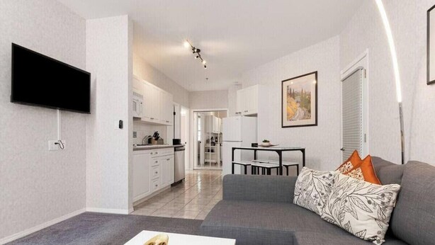 A modern living room with a grey sofa, a flat-screen TV mounted on the wall, a dining area with a table and chairs, and a kitchen in the background. - SUNCHASER VACATION VILLAS / RIVERSIDE B UNIT / GREAT VIEWS / JUNE 28 - JULY 5 (Fairmont Hot Springs)