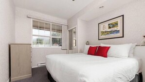 A hotel room with a bed, a window, a door, and a wall-mounted picture. - SUNCHASER VACATION VILLAS / RIVERSIDE B UNIT / GREAT VIEWS / JUNE 28 - JULY 5 (Fairmont Hot Springs)
